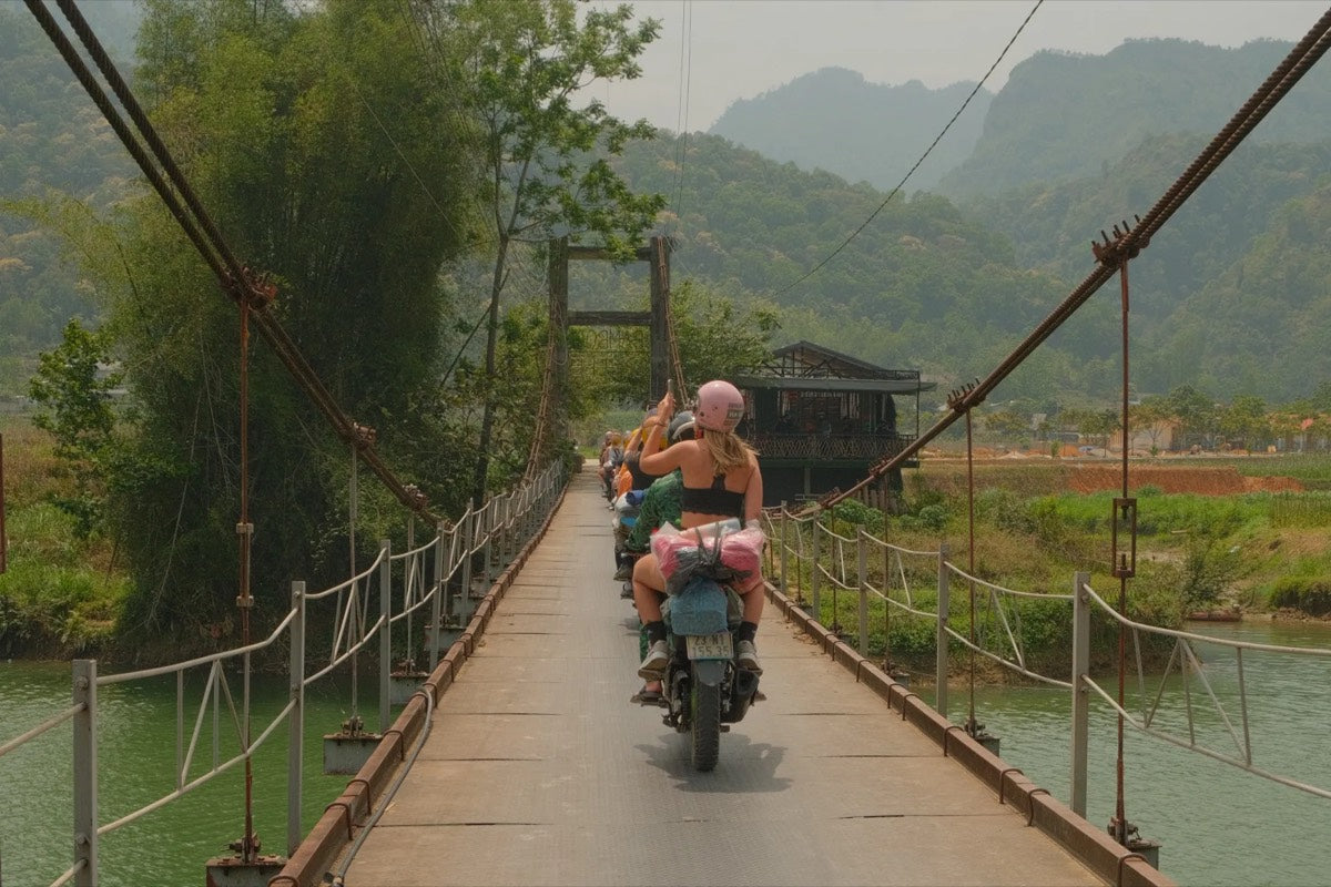 Riding motorbikes in a line across a suspension bridge in the mountains of northern Vietnam